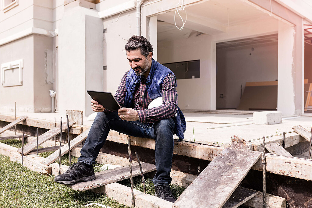 Mann an einem Rohbau mit Tablet in der Hand