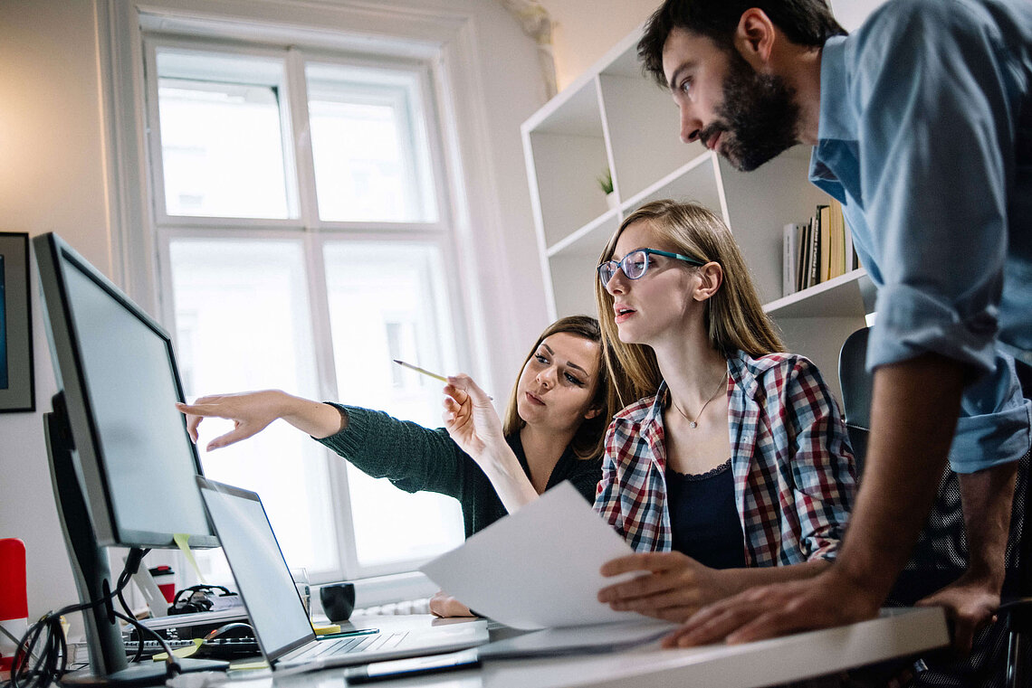 Personen im Büro schauen auf Monitor und zeigen darauf