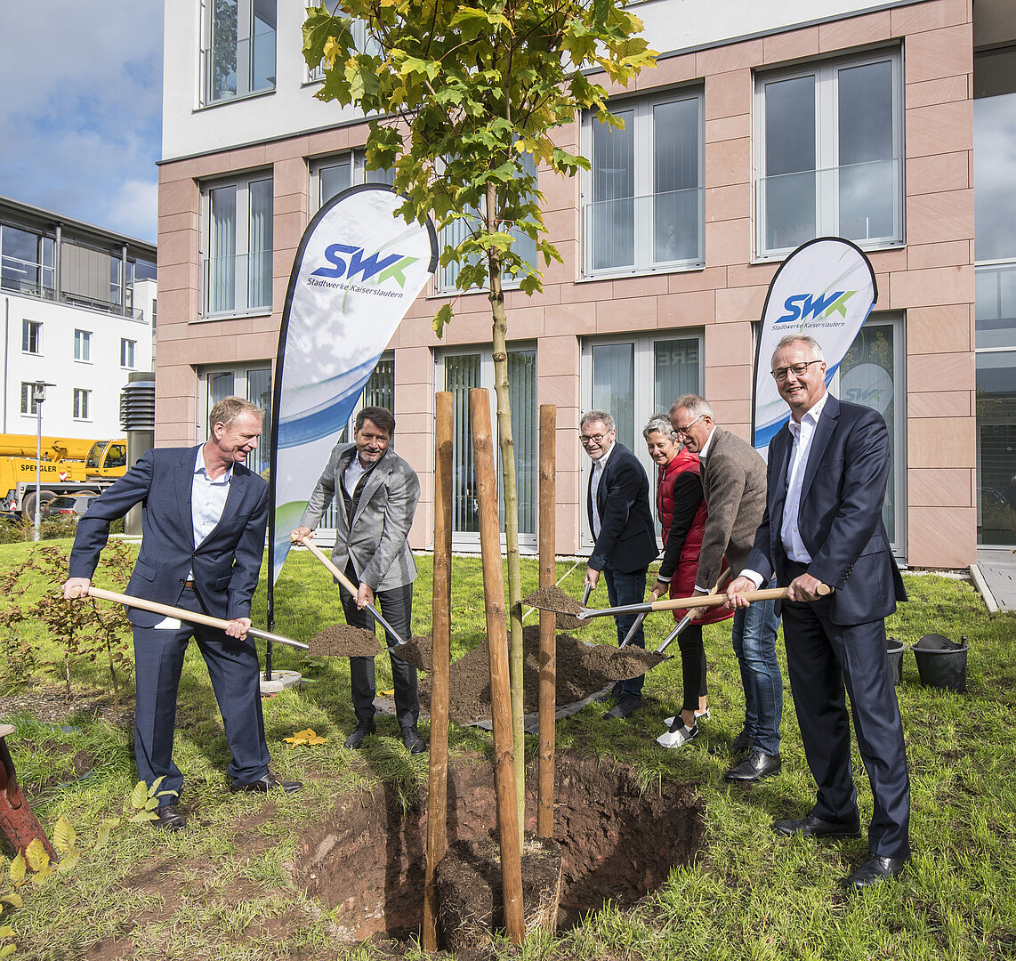 SWK-Mitarbeiter und weitere Personen stehen mit Schaufeln in der Hand um einen gepflanzten Baum herum im PRE-Park