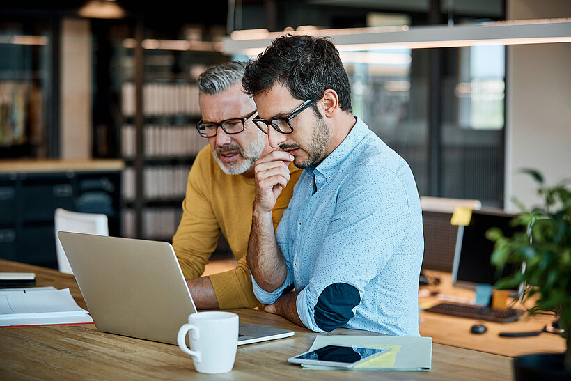 Männer schauen auf Laptop im Büro