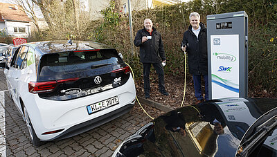 SWK E-Ladestation Dansenberg und einem SWK-Auto auf dem Parkplatz, Personen stehen neben Ladestation mit Ladestecker und SWK-Ladekarte in Hand 