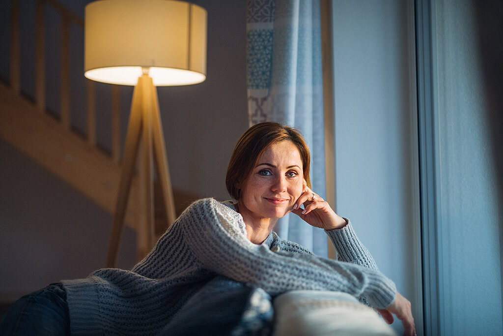 Frau auf Couch am Fenster schaut in die Kamera