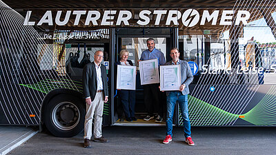 Vier Personen stehen vor und in der Tür eines Busses. Drei von ihnen halten Bilderrahmen mit den Zertifikaten in der Hand.