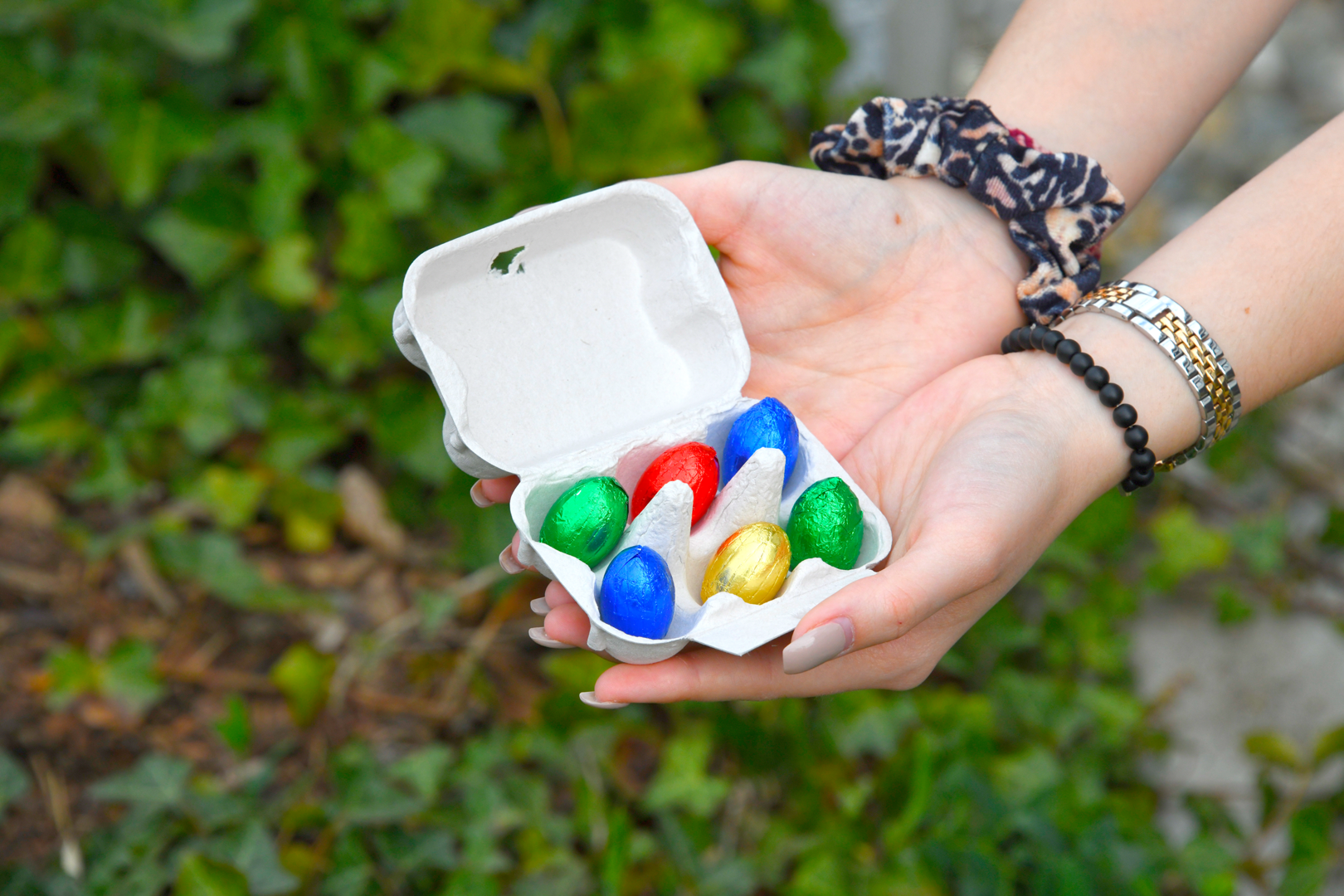 In Händen wird eine Eierschachtel mit bunt-verpackten Schokoladen-Eiern gehalten