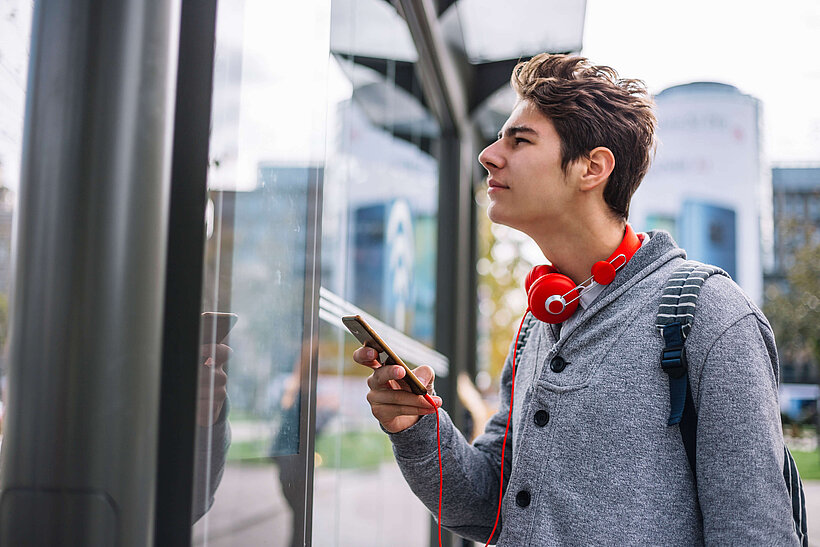 Mann mit Handy in der Hand und Kopfhörer schaut nach Fahrplanauskunft