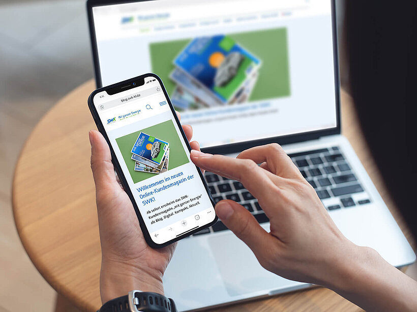Eine Hand hält ein Smartphone. Darauf zu sehen ist die Startseite des SWK Blog. Im Hintergrund ist ein Laptop auf dem Tisch. Darauf zu sehen ist die Startseite des SWK Blog.