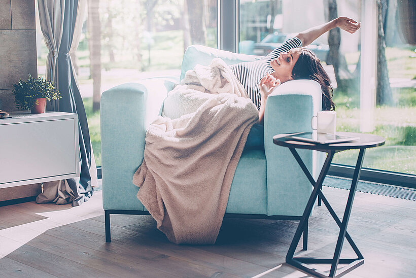 Frau auf Sessel mit einer Decke zugedeckt an einem Fenster 