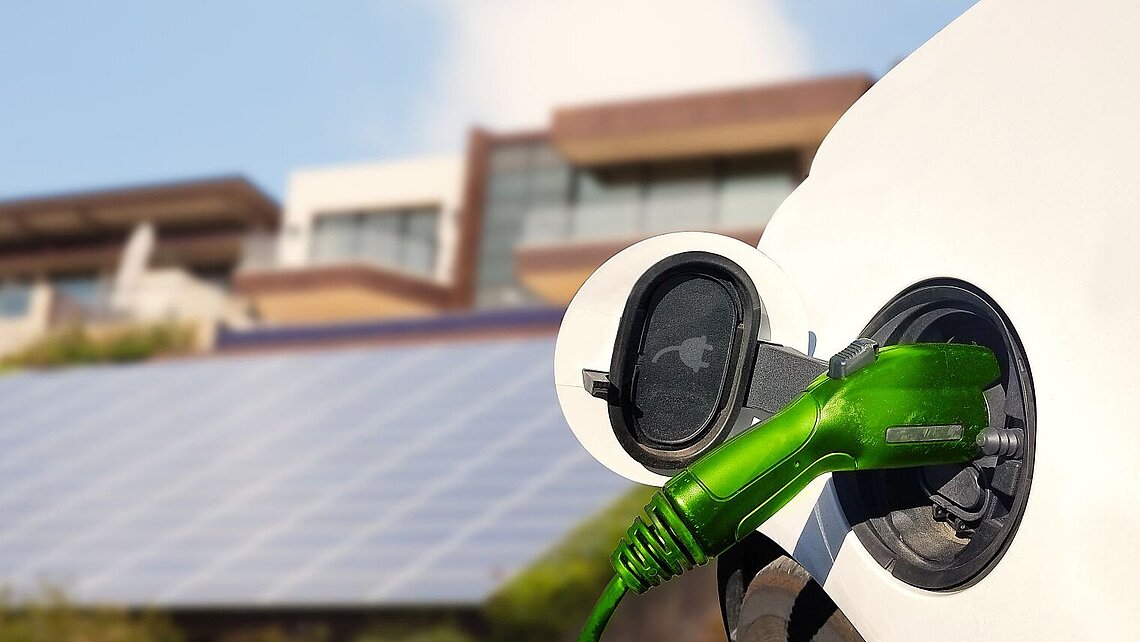 Auto am Laden vor Gebäuden und Photovoltaik-Anlagen