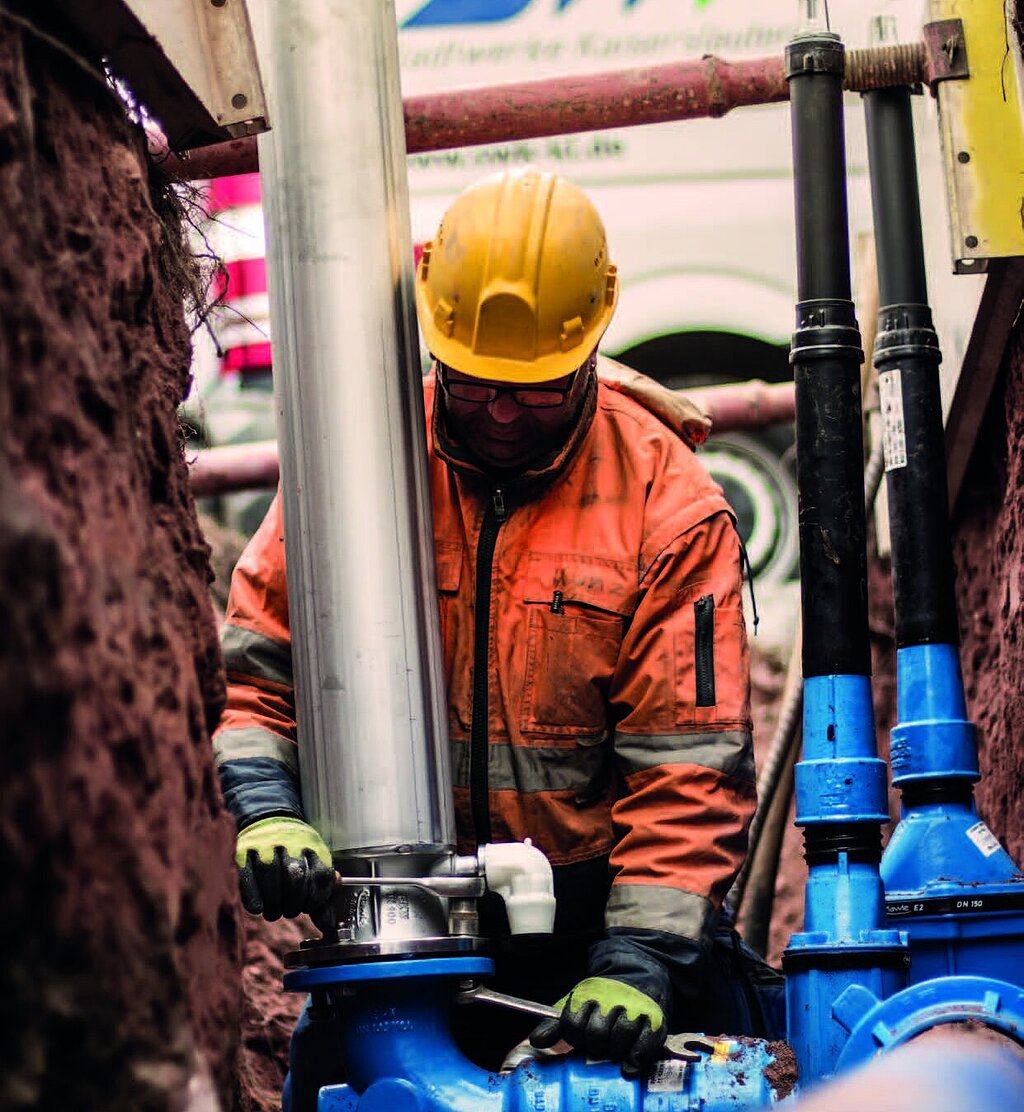 Mann arbeitet an einem Rohr an Baustelle, im Hintergrund SWK-Transporter